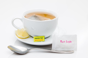 A cup of green tea with sugar and lemon wedge.