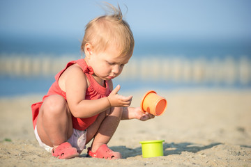 Baby playing on the sandy beach near the sea. Cute little girl in red dress with sand on tropical beach. Ocean coast.