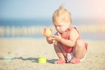 Baby playing on the sandy beach near the sea. Cute little girl in red dress with sand on tropical beach. Ocean coast.