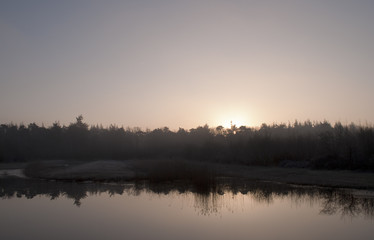 Obraz premium A winter morning landscape with reflection in the lake and upcomming sun.