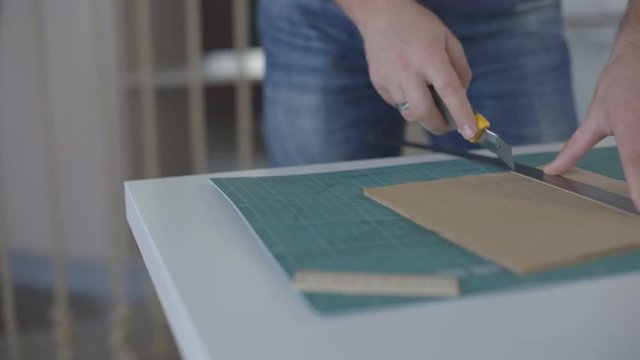 It is close-up image of man cutting paper with stationary knife
