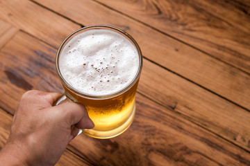 hand holding beer in mug glass on wood table