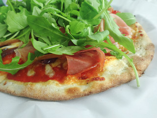 Fresh tasty pizza with prosciutto ham, arugula, tomato sauce, onions, olives and mozzarella cheese. Close up.