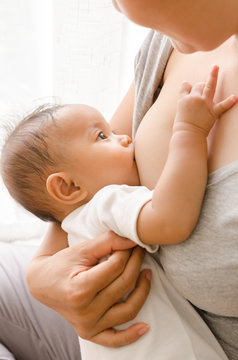 Mother breastfeeding her newborn baby beside window