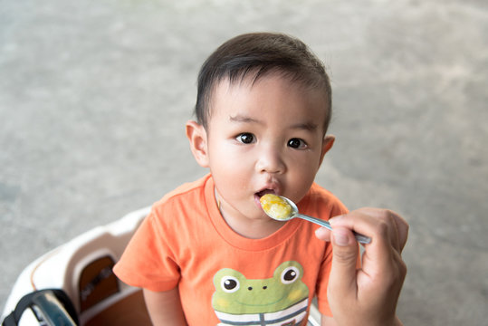 Little Asian Baby Eating Rice Porridge In Smile