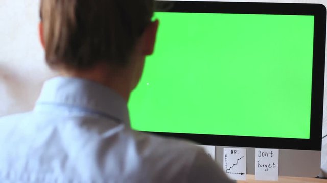 A freelancer working on a computer plastered with notes, reminders, stickers. On the monitor green screen, chroma key.