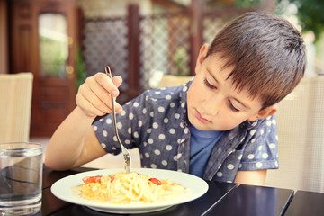 Cute boy eating spaghetti in cafe