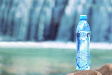 Bottle with fresh water on waterfall  background