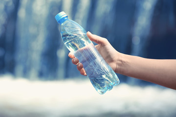 Woman hand holding bottle with fresh water on waterfall  background