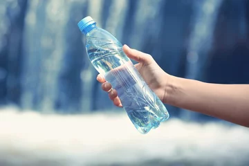 Foto op Plexiglas Vrouw hand met fles met zoet water op waterval achtergrond © Africa Studio