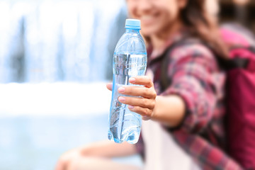 Woman holding bottle with fresh water on waterfall  background