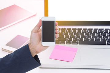 Hand holding mobile phone with office table background