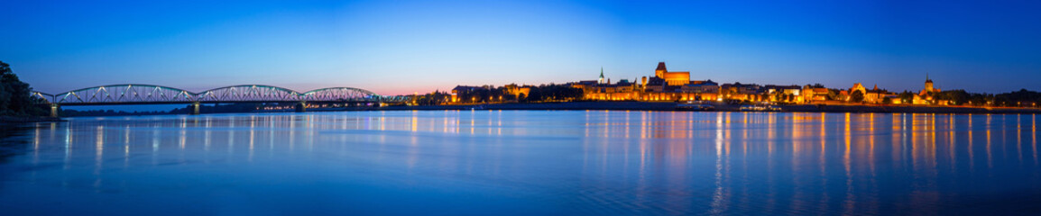 Obraz premium Panorama of Torun at night reflected in Vistula river, Poland