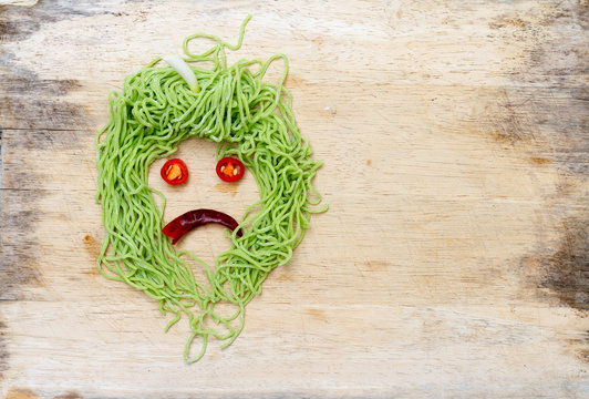 sad faces on wood background made from vegetable and noodle with