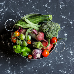 Assortment of fresh vegetables - broccoli, zucchini, tomatoes, peppers, green beans, beets, garlic in a metal basket on dark background