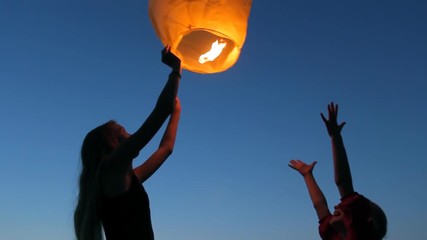 Two young girls launching a Chinese sky fly fire lantern to make a wish, summer holidays, celebration, family, children - Powered by Adobe