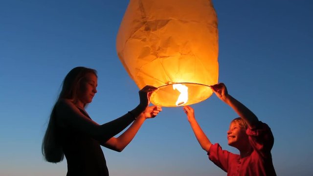 Children girls holding sky lantern to make wish. Two sisters launching flying paper hot air balloon