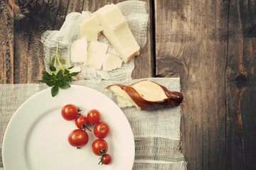 Cherry tomatoes on a white plate with basil, Parmesan cheese and one half of a bread bun on a sterile gauze, wooden table background. Toned, horizontal 