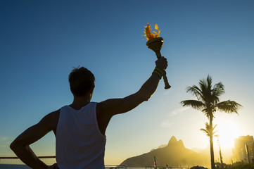 Silhouette of torchbearer athlete standing with sport torch in front of the Rio de Janeiro, Brazil...