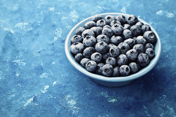 Great bilberry or blueberry in plate on blue rustic background. Vintage style.