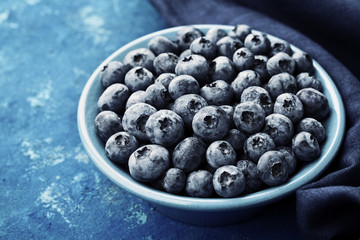 Great bilberry or blueberry in bowl on blue rustic background. Vintage style.