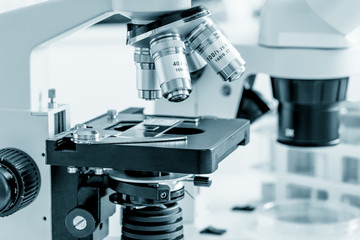 Science microscope on lab bench. Microbiology laboratory. Blue toned image of binocular microscope
