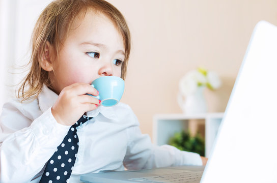 Toddler girl drinking from a mug in front of a laptop