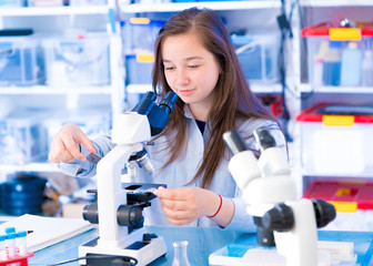Teen girl in school laboratory. University nature science lab. Researcher working with binocular...