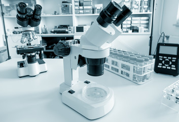 Science microscope on lab bench. Microbiology laboratory. Blue toned image of binocular microscope