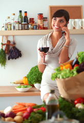 Young woman cutting vegetables in kitchen, holding a glass of wine