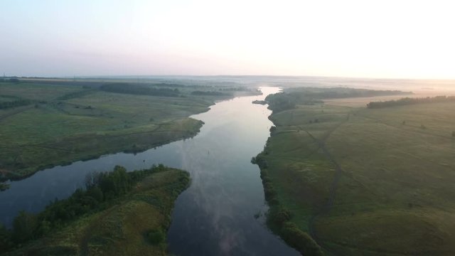 Aerial video of a big lake at sunrise while fog creeping over the water. Cranes fly over the lake. Drone moving forward. 4K Aerial stock footage shot at summer season time.
