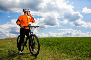Fototapeta premium Young Cyclist In Orange Shirt Checks His Phone