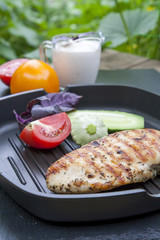 Grilled chicken breast steak with tomato, cucumber and violet basil on teflon pan grill, black slate stone, summer background