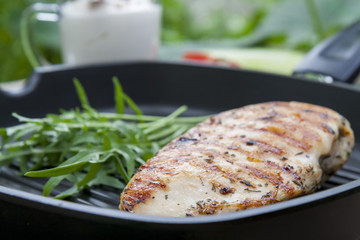 Grilled chicken breast steak with arugula rucola on teflon pan grill, black slate stone background