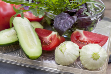 Different ripe organic vegetables tomatoes, cucumber and patty pan squash, fresh arugula and violet basil on a tray