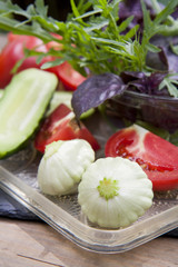 Different ripe organic vegetables tomatoes, cucumber and patty pan squash, fresh arugula and violet basil on a tray
