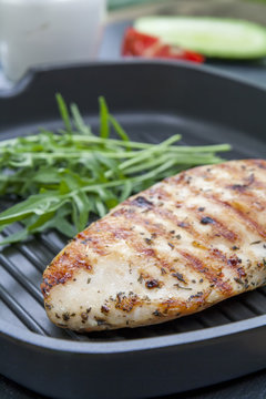 Grilled chicken breast steak with arugula rucola on teflon pan grill, black slate stone background
