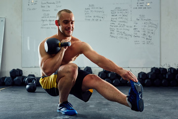 Happy athlete doing one leg situps with kettlebell at the gym