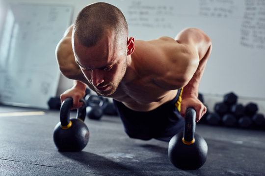 Closeup of athletic man doing kettlebell pushups at the gym - Powered by Adobe