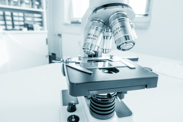 Science microscope on lab bench. Microbiology laboratory. Blue toned image of binocular microscope