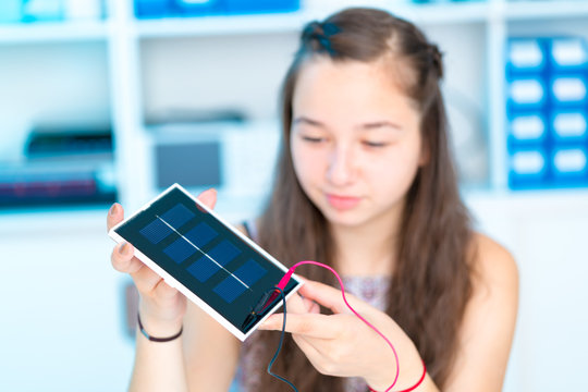schoolgirl with solar cell in hand in physics classroom