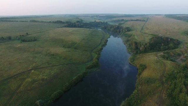 Aerial video of a big lake at sunrise while fog creeping over the water. Drone moving forward. 4K Aerial stock footage shot at summer season time.
