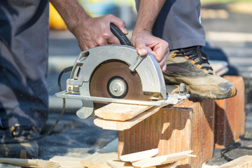 Close up of hands using circular saw outdoors
