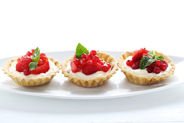 Dessert tartlets with berries on white wooden background