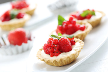 Dessert tartlets with berries on white wooden background