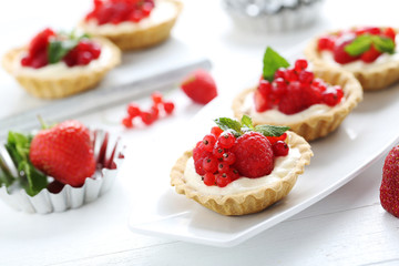 Dessert tartlets with berries on white wooden background