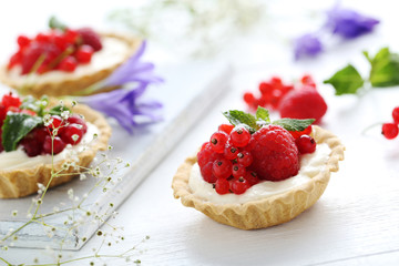 Dessert tartlets with berries on white wooden background