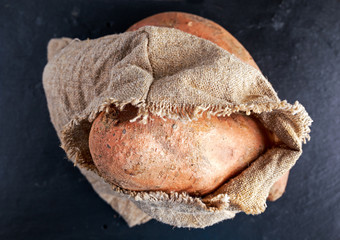 Obraz premium Freshly harvested organic sweet potatoes in a burlap bag on wooden table.
