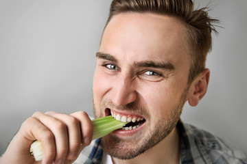 Handsome man eating celery on grey background