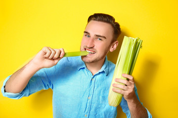 Handsome man eating celery on yellow background © Africa Studio